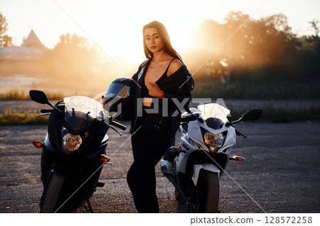 Between two vehicles, against smoke. Woman is with motorcycle outdoors Between two vehicles, against smoke. Woman is with motorcycle outdoors 128572258