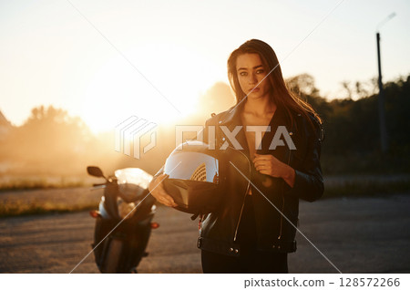 Sunset time, smoke is behind. Woman is with motorcycle outdoors Sunset time, smoke is behind. Woman is with motorcycle outdoors 128572266