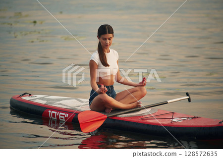 Sitting in lotus pose. Young woman is on sup boards in the lake Sitting in lotus pose. Young woman is on sup boards in the lake 128572635