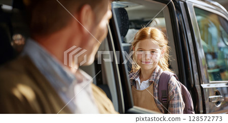 Happy young student with a backpack smiles at a parent from inside a car, capturing a sweet moment of a morning school drop-off and family connection 128572773