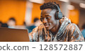 A young man wearing headphones is intently focused on his laptop, suggesting deep concentration while studying, working, or enjoying multimedia content in a modern setting. 128572887