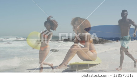 Image of biracial female surfer over female surfer at beach Image of biracial female surfer over female surfer at beach 128573112