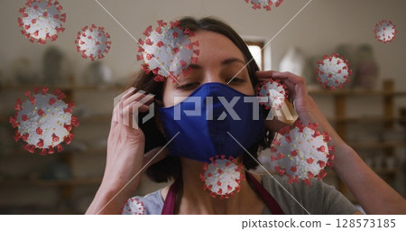 Image of covid 19 cells over woman working in pottery studio putting face mask on Image of covid 19 cells over woman working in pottery studio putting face mask on 128573185