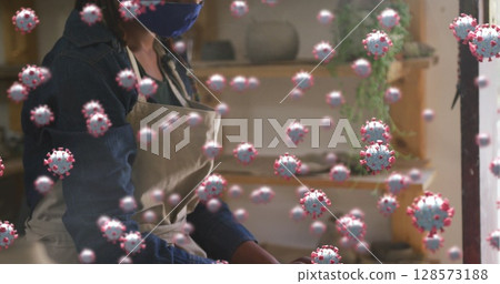 Image of virus cells over african american woman with face mask forming pottery Image of virus cells over african american woman with face mask forming pottery 128573188