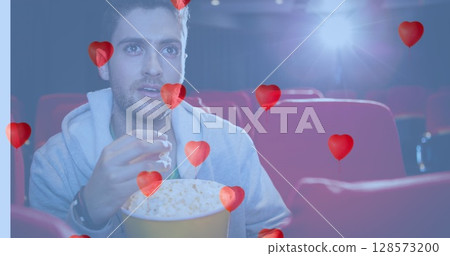 Image of heart icons over caucasian man eating popcorn in cinema 128573200