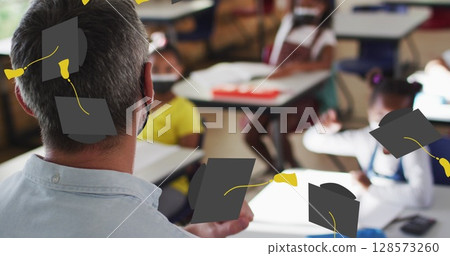 Image of graduation cap icons over diverse schoolchildren and teacher wearing face masks 128573260