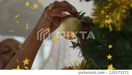 Image of stars over african american woman decorating christmas tree 128573271