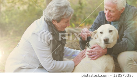Spot of light against caucasian senior couple playing with their dog in the garden Spot of light against caucasian senior couple playing with their dog in the garden 128573383