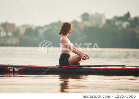 Sitting in lotus pose. Young woman is on sup boards in the lake Sitting in lotus pose. Young woman is on sup boards in the lake 128573500