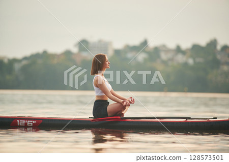 Sitting in lotus pose. Young woman is on sup boards in the lake Sitting in lotus pose. Young woman is on sup boards in the lake 128573501