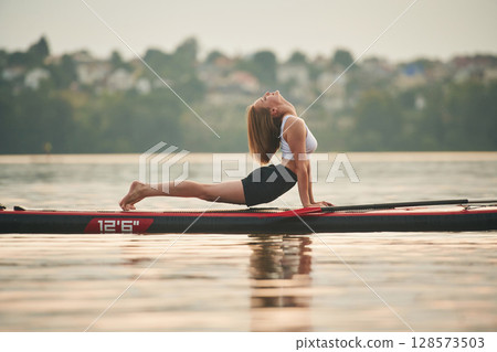 Doing fitness exercises. Young woman is on sup boards in the lake 128573503