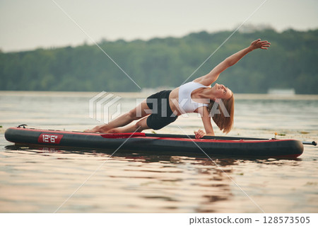 Doing fitness exercises. Young woman is on sup boards in the lake Doing fitness exercises. Young woman is on sup boards in the lake 128573505