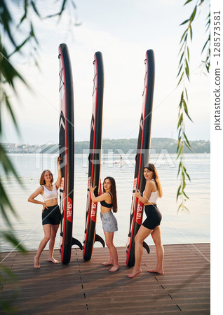 Green leaves. Women are standing with sup boards against the lake 128573581