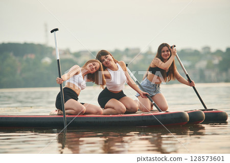 Friends are sitting and having fun. Young women are on sup boards in the lake Friends are sitting and having fun. Young women are on sup boards in the lake 128573601