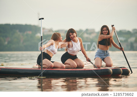 Friends are sitting and having fun. Young women are on sup boards in the lake Friends are sitting and having fun. Young women are on sup boards in the lake 128573602