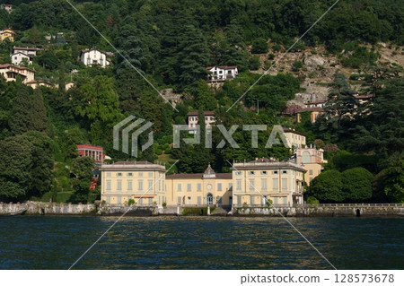 Luxurious historic villas on the shores of Lake Como in Italy, surrounded by dense greenery and mountains. Luxurious historic villas on the shores of Lake Como in Italy, surrounded by dense greenery and mountains. 128573678