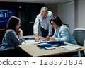 Senior executive mentoring junior colleague in modern office with presentation screen 128573834