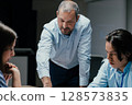 Senior executive mentoring junior colleague in modern office with presentation screen 128573835