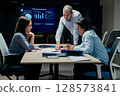 Senior executive mentoring junior colleague in modern office with presentation screen 128573841