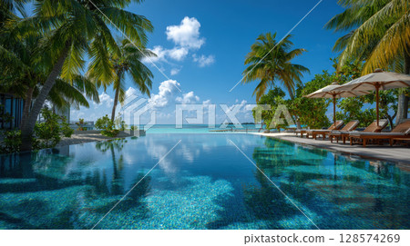 An exquisite view of a tropical paradise featuring an infinity pool merging seamlessly with the crystal-clear ocean, framed by lounge chairs and a palm tree, embodying ultimate relaxation 128574269