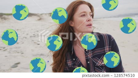 Image of falling globes over caucasian woman picking up rubbish from beach 128574510