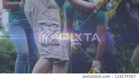 Image of lights over diverse volunteer group picking up rubbish in countryside 128574567