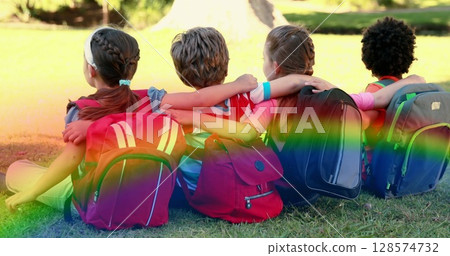 Image of rainbow fog over diverse children sitting on grass 128574732