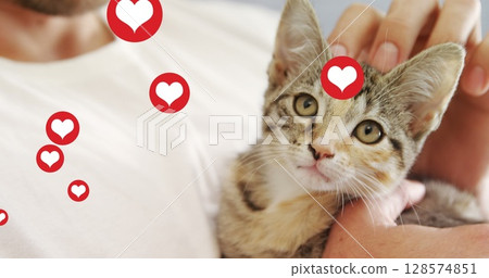 Multiple heart icons floating against mid section of a man playing with his kitten 128574851