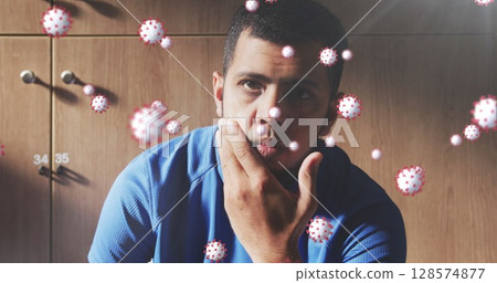 Image of virus cells floating over biracial male football player in changing room 128574877