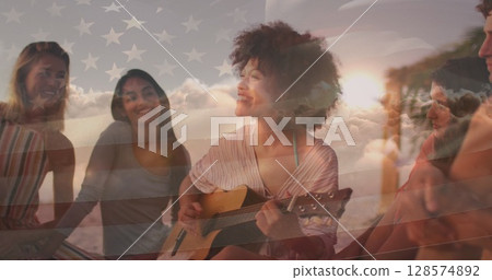 Image of flag of united states of america over happy biracial woman playing guitar on beach 128574892