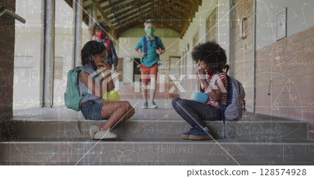 Image of mathematical equations over diverse schoolchildren wearing face masks 128574928