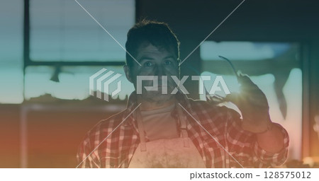 Image of light spot over caucasian male worker smiling and wearing safety goggles in workshop 128575012