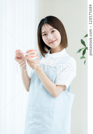 Dental staff woman holding a toothbrush and a tooth model 128575084