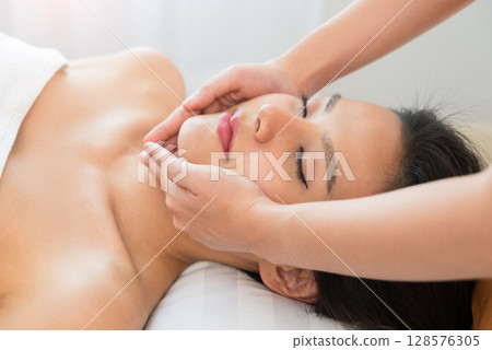 Face massage. Young woman with closed eyes getting spa facial massage treatment at spa salon 128576305