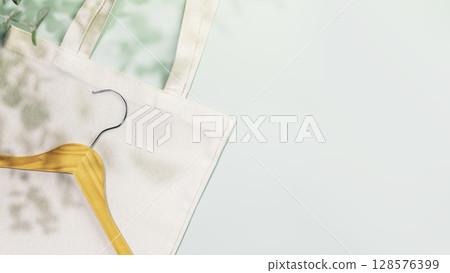 Sustainable shopping, buying or sales concept. Eco friendly still life with wooden hanger on white textile shopping bag on blue background with plant shadows. Flat lay, copy space Sustainable shopping, buying or sales concept. Eco friendly still life with wooden hanger on white textile shopping bag on blue background with plant shadows. Flat lay, copy space 128576399