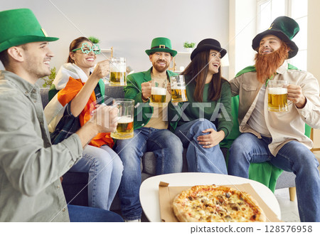 Happy friends celebrating Saint Patrick's Day eating pizza and drinking beer at home. Happy friends celebrating Saint Patrick's Day eating pizza and drinking beer at home. 128576958