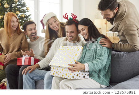 Woman sitting at home with friends on Christmas eve opening big present box celebrating New Year 128576981