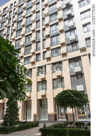 Downtown district with trees and lawn. High rise building on sunny day. Modern architecture. Business office building. Geometric lines in architecture. Modern building exterior. Modern street view. Downtown district with trees and lawn. High rise building on sunny day. Modern architecture. Business office building. Geometric lines in architecture. Modern building exterior. Modern street view. 128577040