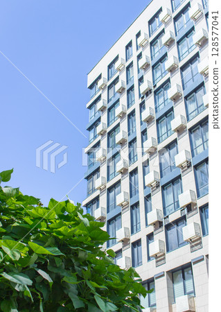 Downtown district with trees and lawn. High rise building on sunny day. Modern architecture. Business office building. Geometric lines in architecture. Modern building exterior. Modern street view. Downtown district with trees and lawn. High rise building on sunny day. Modern architecture. Business office building. Geometric lines in architecture. Modern building exterior. Modern street view. 128577041