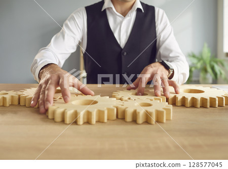 Business man connecting big wooden gears sitting at the desk solving the problem in office. 128577045