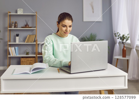 Happy woman sitting at home with laptop on writing desk, close-up 128577099