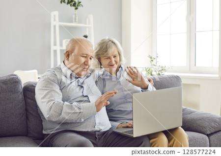 Elderly Couple Using Laptop for Video Call and Waving Greetings 128577224