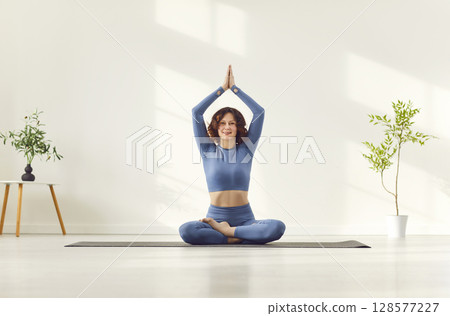 Attractive woman meditating, girl with raised arms up to make Namaste gesture seated in lotus pose  128577227
