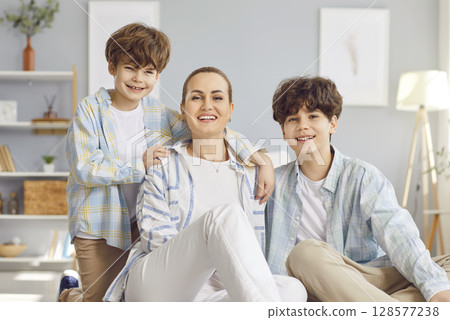 Happy family mother and two sons enjoying leisure time, embracing, looking at camera and smiling. 128577238