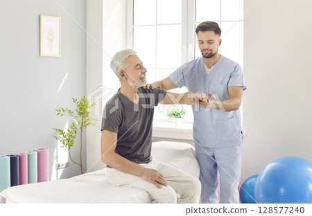 Chiropractor or physical therapist working with senior man's arm in rehabilitation hospital. 128577240