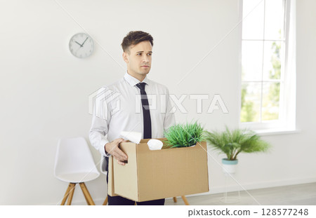 Upset dismissed business man in formal clothes with a box of belongings moving his office. 128577248