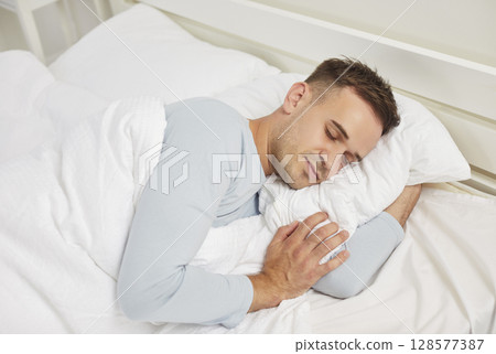 Man sleeping on his side on a soft white pillow in a comfortable bed in the bedroom Man sleeping on his side on a soft white pillow in a comfortable bed in the bedroom 128577387