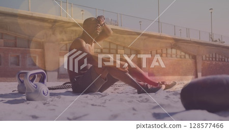 Spots of light against tired african american fit man taking a break from working out at the beach Spots of light against tired african american fit man taking a break from working out at the beach 128577466