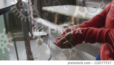 Image of covid 19 cells and icons over biracial woman sanitizing her hands 128577537