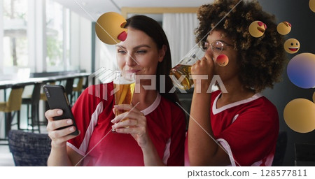 Image of emoji icons over happy diverse female friends using smartphone with beer 128577811